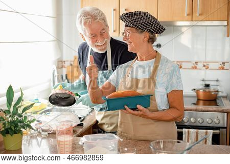 Smiling Older Woman Holding Her Freshly Baked Homemade Plumcake With Thumb Up While Her Husband Wash