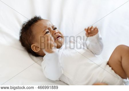 Portrait Of Crying Little Black Baby Wearing Bodysuit Lying On Bed
