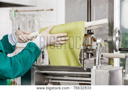 Cropped image of male chef wrapping pasta sheet on rolling pin into machine at commercial kitchen