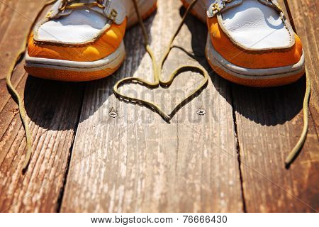  a pair of deck shoes on a nice wooden porch with the laces in a heart shape on a bright sunny day toned with a retro vintage instagram filter effect 