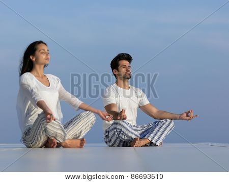 young couple practicing yoga at sunset in modern home terace with ocean and sunset in background