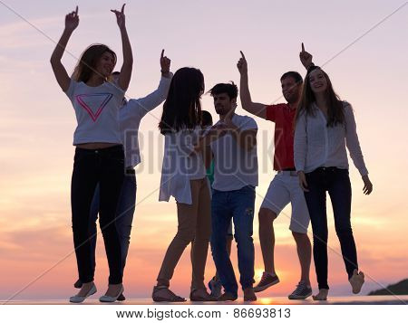 group of happy young people dancing and have fun on party in modern home bacony with sunset and ocean in background
