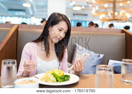 Woman looking at the cellphone and having her lunch in restauarant