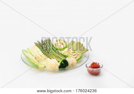 Grilled zucchini and asparagus, broccoli, lobi and cauliflower on a glass plate with red sauce