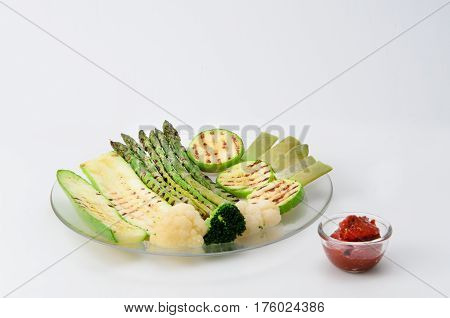 Grilled zucchini and asparagus, broccoli, lobi and cauliflower on a glass plate with red sauce
