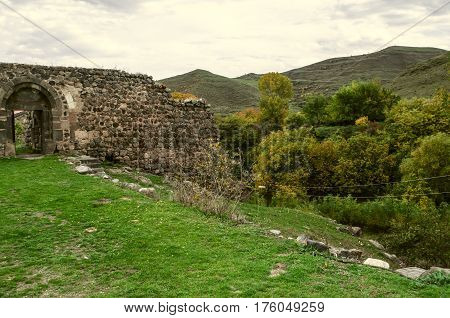 Entrance to the stone wall medieval monastery about garden with yellowed the walnut trees