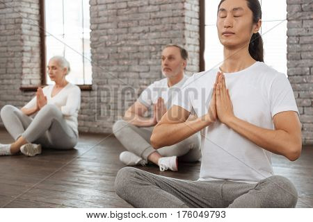 Do yoga. Group of healthy people crossing their legs while sitting on the floor holding hands together in front of chest