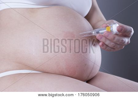 Pregnant woman making injection in stomach close-up studio shot on gray background