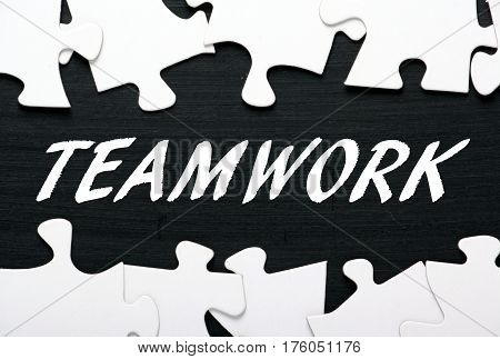 The word TEAMWORK in white text on a blackboard with jigsaw puzzle pieces as a concept for finding solutions to team building in business
