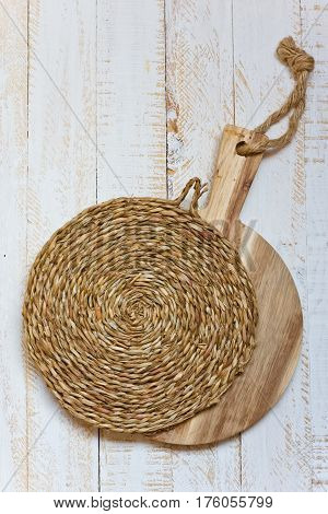 Wood round cutting board and wicker rattan coaster on white plank wood background rustic kitchen interior Provence style minimalistic kinfolk top view