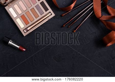 Makeup cosmetics, everyday palette frame on black background. Top view, flat lay with copy space. Beauty tools pastel beige and terracota colors collection, lipstick, brush, eyeshadow