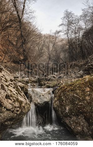 A small waterfall on a mountain small river in a beautiful autumn forest with a fog