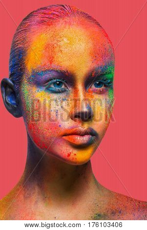 Bold color fantasy. Holi festival of colors background. Female face art with creative make up. Closeup studio portrait of young fashion model isolated on peach pink background