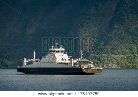 Norwegian ferry in sunlight wits steep mountain slope background. Sunset sun beams. Sognefjorden, Norway.