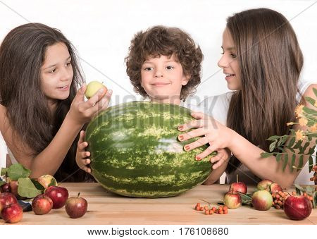 Children playing with fruits sitting at the table. Gray background. Close-up.