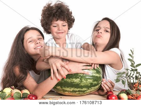 Brother and two sisters fighting over a huge watermelon sitting at the table. White background. Close-up.