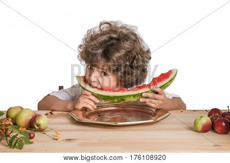 Little curly boy eating large ripe watermelon. Blue background. Close-up.