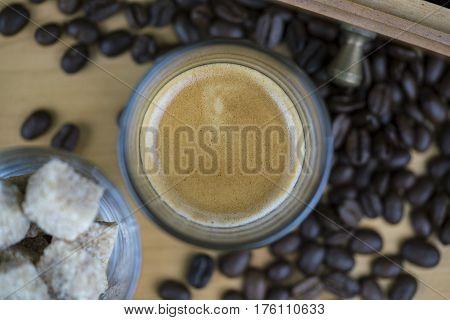 Cup of frothy hot coffee with beans and crystallised sugar cubes viewed from above with focus to the surface of the beverage