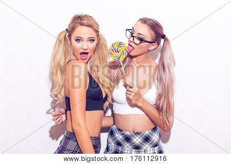Sexy woman in glasses licking lollipop with surprised girlfriend retro style