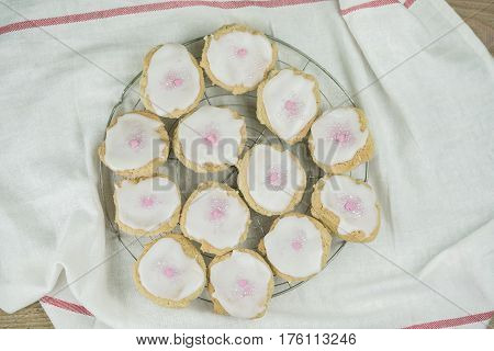 Batch of freshly baked homemade cookies on a wire tray in the kitchen topped with white icing and little pink candy hearts for Valentines or an anniversary