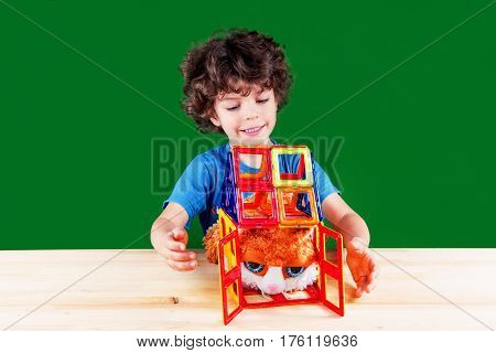 The brown-eyed curly-headed kid sets free a cat with eyes big for the fear which has got into the house. On a green background.