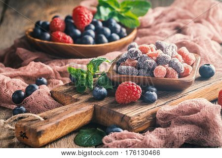 Dried and candied fruits and berries in wooden bowl with fresh raspberry and blueberry