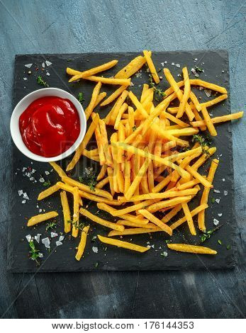 French fries with sea salt, cracked pepper and ketchup on stine board.