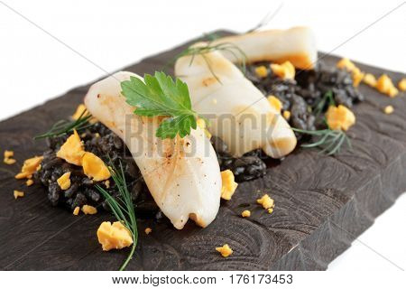 Black squid ink rice and fried calamar on wooden serving board, close-up
