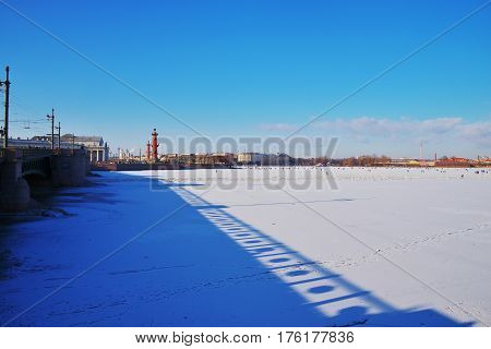 Winter landscape of St. Petersburg. View of the Neva is covered with ice, Palace bridge, Rostral columns. Away people walking on river between Peter and Paul fortress and spit of Vasilyevsky island on a Sunny day.