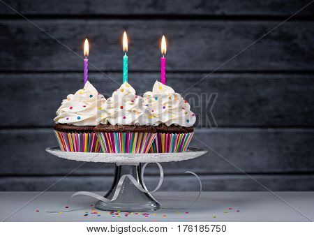 Three chocolate cupcakes with buttercream icing and Birthday candles on a cake stand