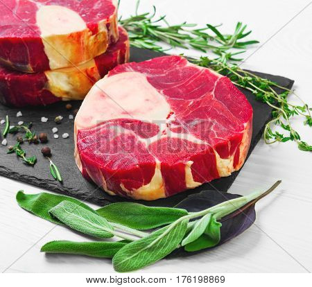 meat beef veal shank slices meat for Osso Buco cooking on white wooden background. Ingredients for beef meat Osso Buco sage leaves thyme rosemary pepper salt pepperl.
