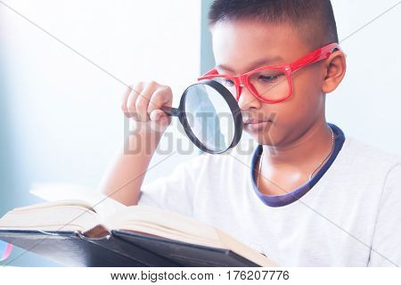 Little boy wearing red glasses reading and using magnifying glass