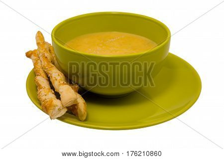 Yellow pumpkin soup in a green plate and crispy italian breadsticks isolated on white