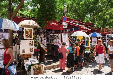 Paris France - Jine 30 2006: Open air artist market at Tertre Square (Place du Tertre) in Montmartre. Tourists considering the menu of a street cafe. Waiters in traditional french costume posing in front of cafe.