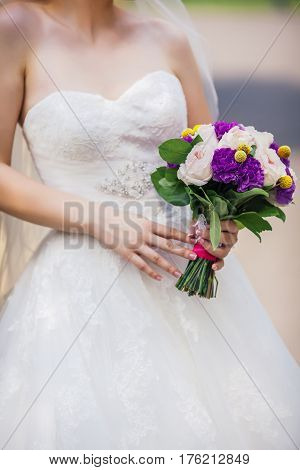 Bride holding delicate and tender marriage bouquet in purple and pink colours with green petals