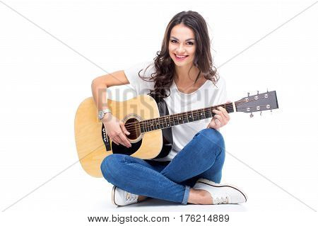 Smiling young woman sitting and playing guitar isolated on white