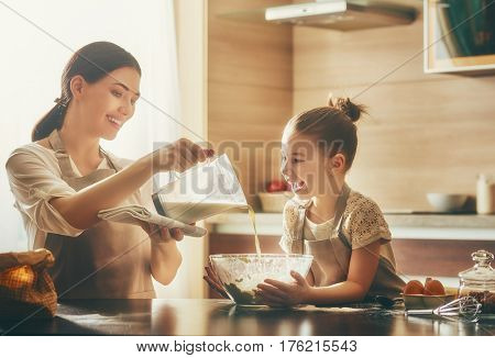 Happy loving family are preparing bakery together. Mother and child daughter girl are cooking cookies and having fun in the kitchen. Homemade food and little helper.