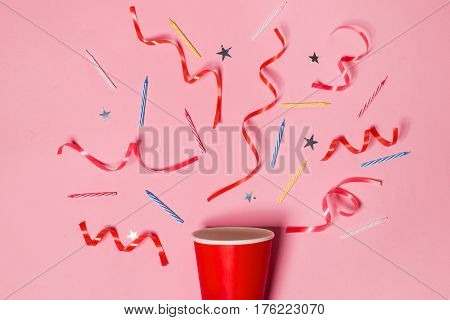 Flat lay of Celebration. Paper cup with colorful party streamers on pink background.
