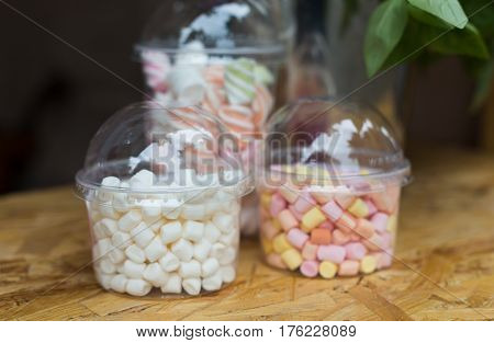 Desserts choice. Marshmallow chewing candies for hot chocolate topping in glass jars on counter bar for sale. Traditional american sweets for sale, closeup