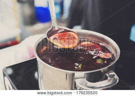 Making mulled wine for sale at country fair. Glintwine with citrus and cloves in big metal stock pot, mixed with soup ladle.