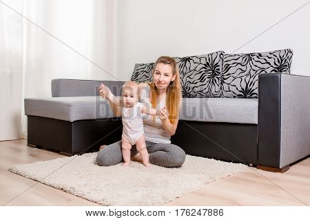 Happy young mother playing with her baby on the floor near the sofa - indoors. Mom with baby at home