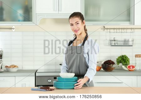 Woman in apron holding dishes on kitchen table