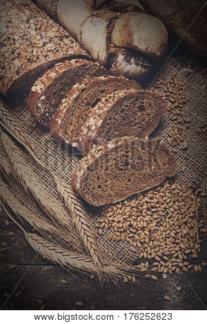 Plenty of sliced bread background. Bakery and grocery concept. Fresh, healthy whole grain sliced rye loaf, sprinkled flour on sack and rustic wood table, food closeup. Vintage filter