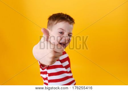 Portrait of a smiling active little boy showing thumbs up isolated over orange background, focus camera on a fist