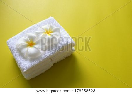 White towel with flowers of plumeria on the yellow background for spa theme.