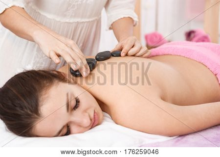 Young cheerful girl working on leg muscles training tramp isolated on white background woman at salon enjoying spa, getting massage with hot stones, lying on massage couch