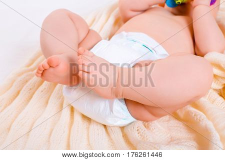 feet of a six months old baby wearing diapers lying in bed at home