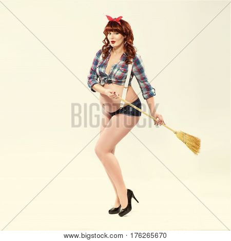 Fashionable redhead pregnant woman in pin up style with broom