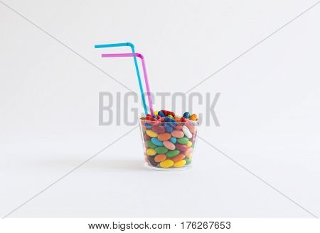 Transparent plastic cup with colorful candy with two blue and pink colored straws on white background.