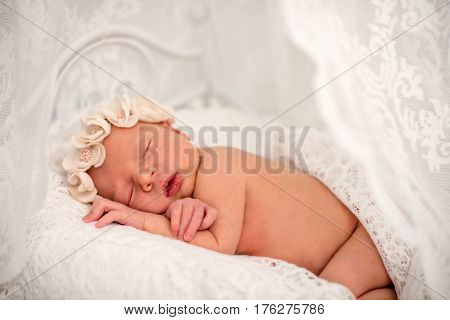 Ideas for newborn photo shoot. Newborn girl sleeping on the tummy to decorative crib. Portrait of a sleeping newborn girl with floral bandage on his head covered with delicate tippet